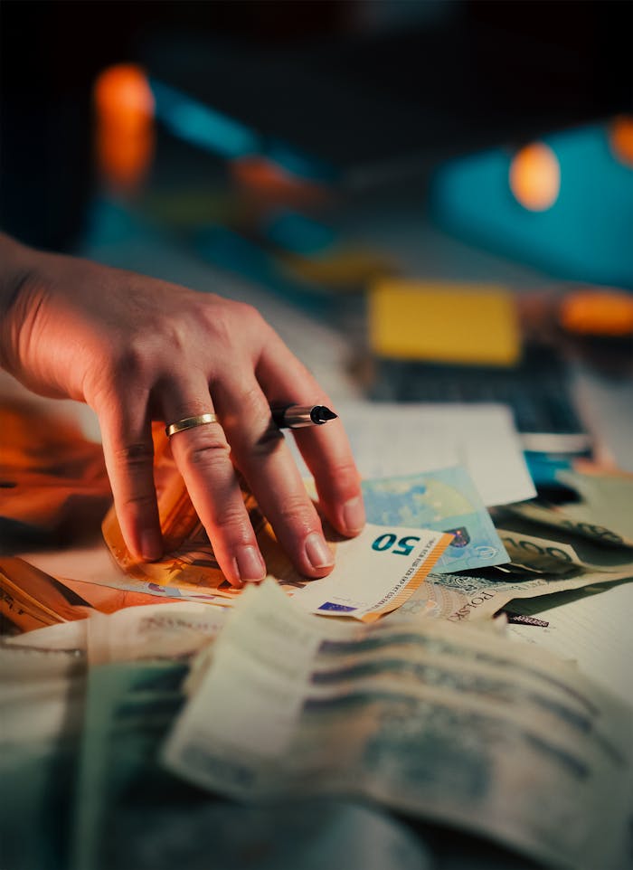 A hand holding euro banknotes over a desk with financial documents and a pen nearby, highlighting finances and legal negotiations.