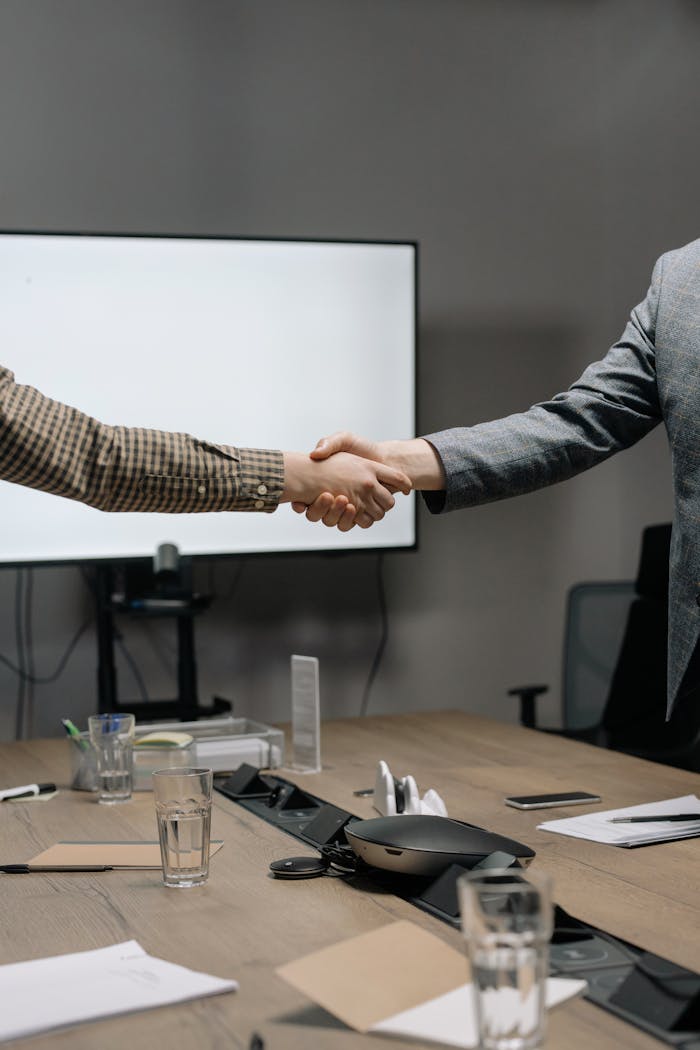 Two business professionals shaking hands in a modern meeting room, symbolizing successful collaboration.